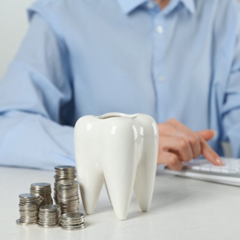 A man calculating the cost of dental crowns with a calculator, coins, and a tooth model